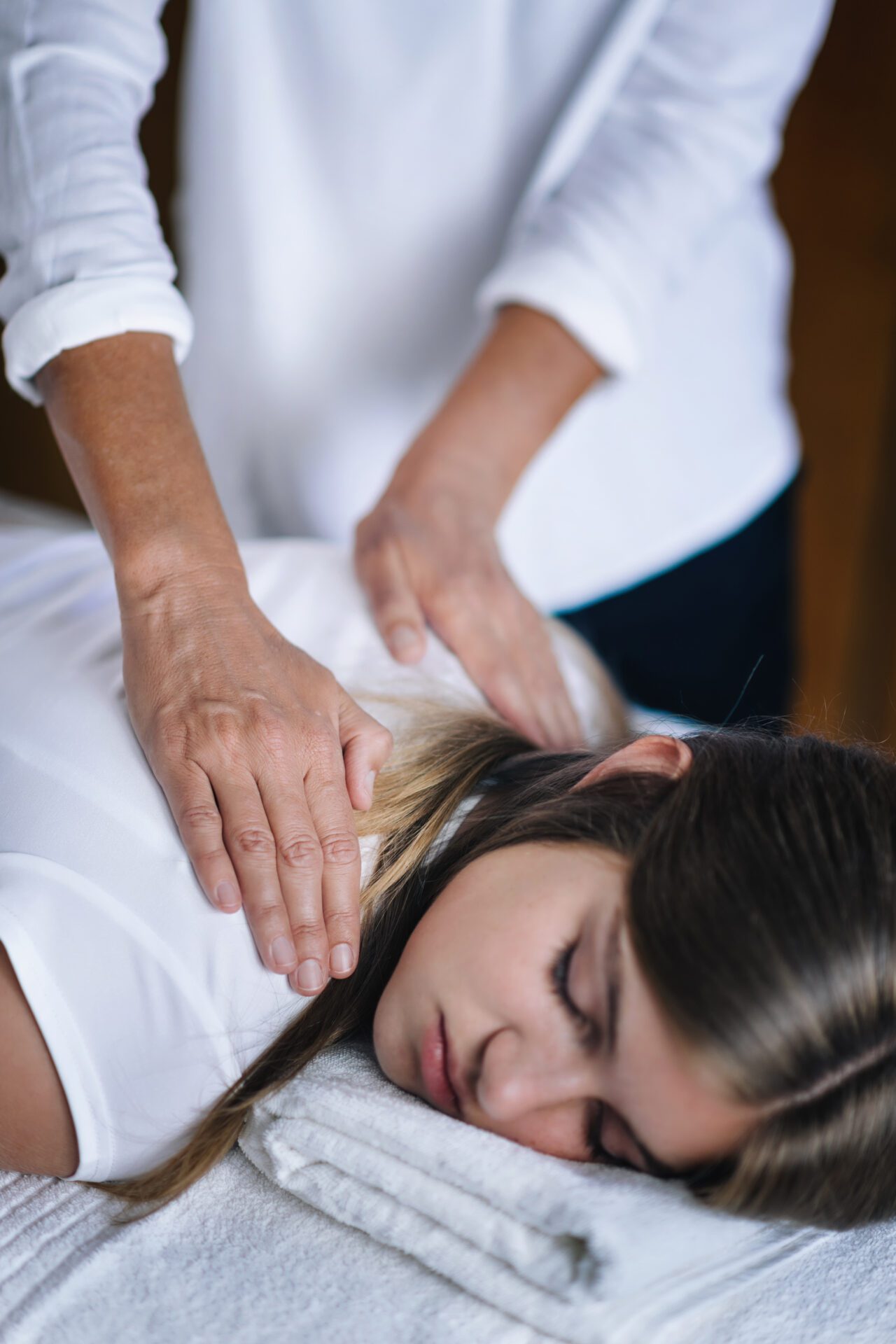 Reiki Shoulders Massage With Peaceful Teenage Girl Vertical image of female Reiki therapist holding hands over shoulders of the patient and transfer energy. Peaceful teenage girl lying with her eyes closed. Alternative therapy concept of stress reduction and relaxation.
